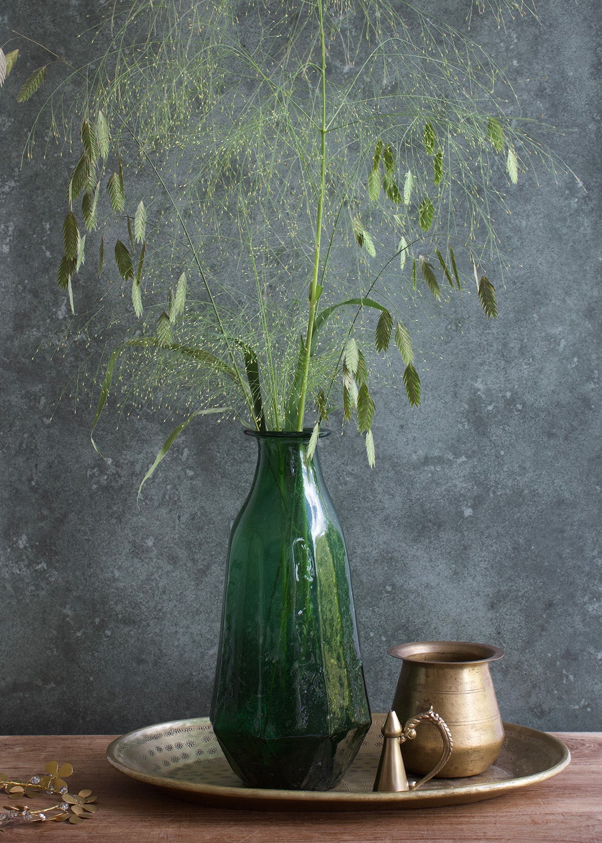 Green vase with plants on a wooden surface against a gray background
