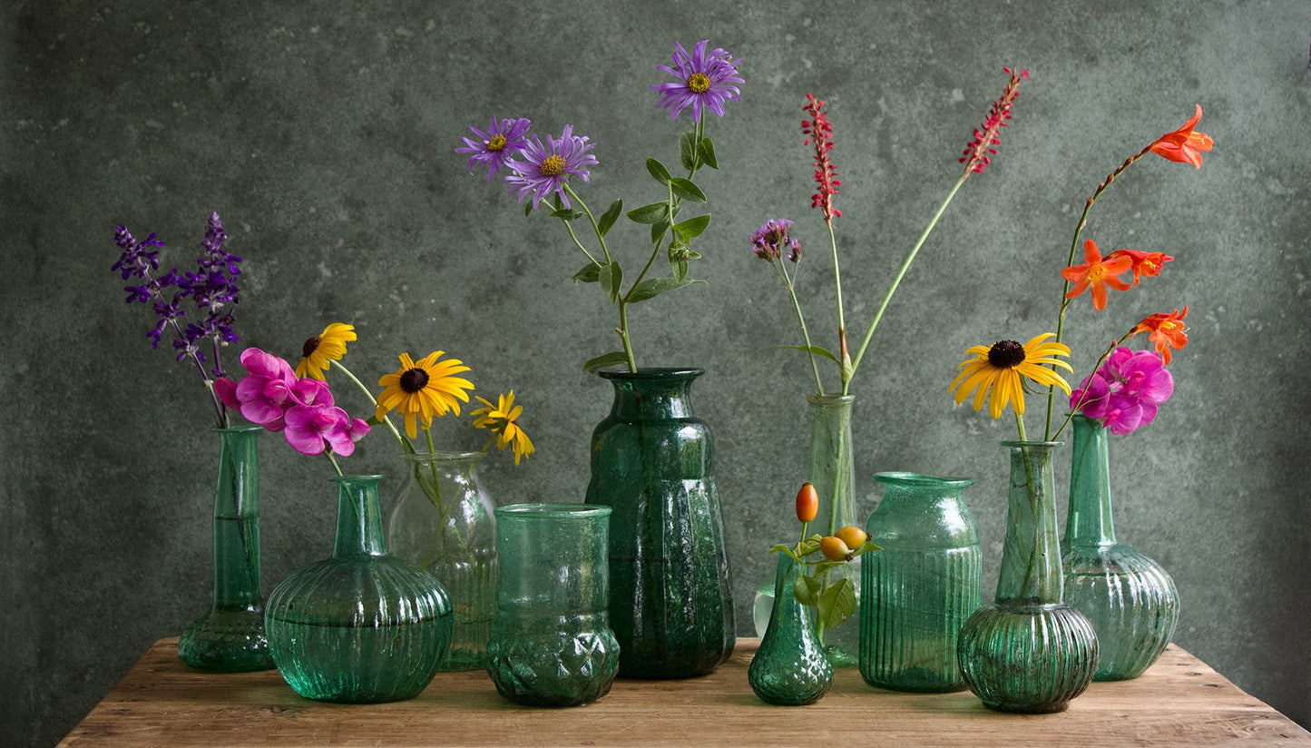 Green glass vases with flowers on a wooden table against a dark gray background