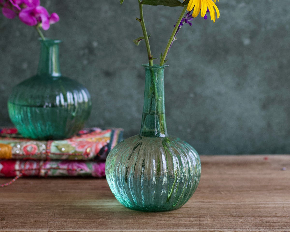 Green ribbed vase with flowers on a wooden surface against a dark background