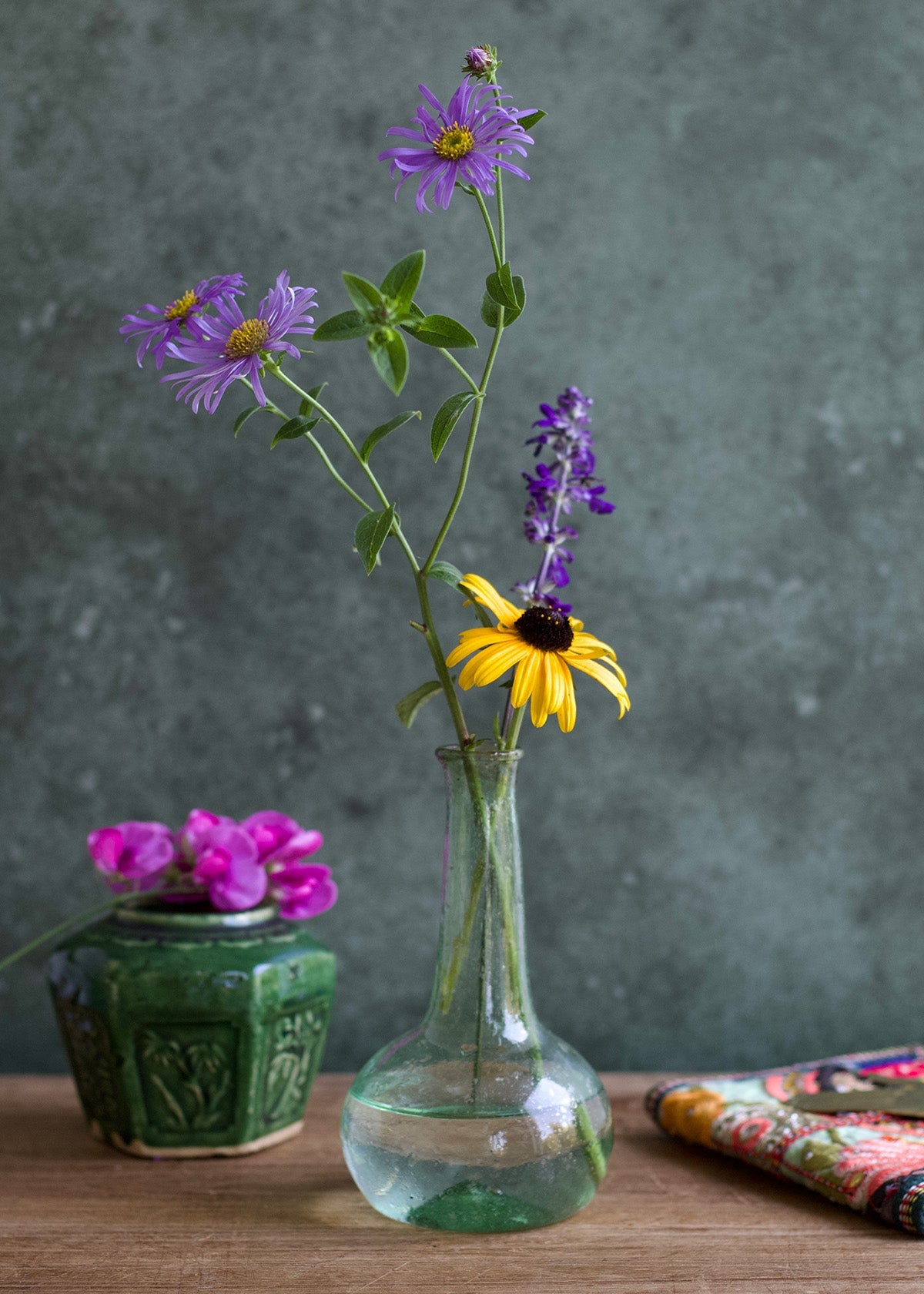 Clear glass vase with purple and yellow flowers on a wooden surface against a gray background