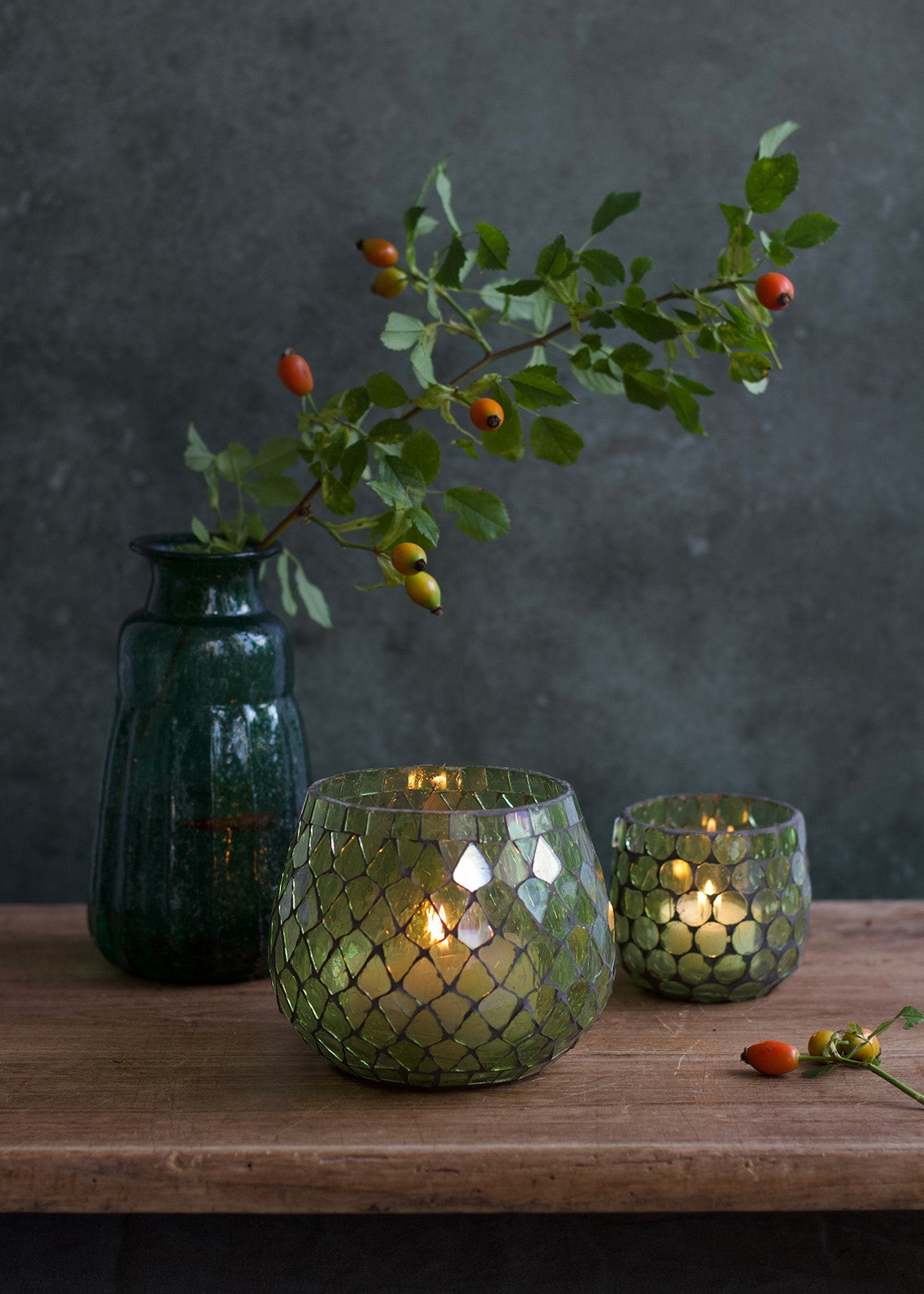 Two green glass candle holders with a dark vase on a wooden surface against a dark background.