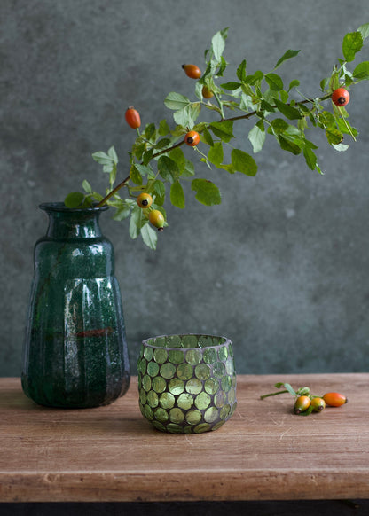 Green vase and glass with a branch on a wooden surface