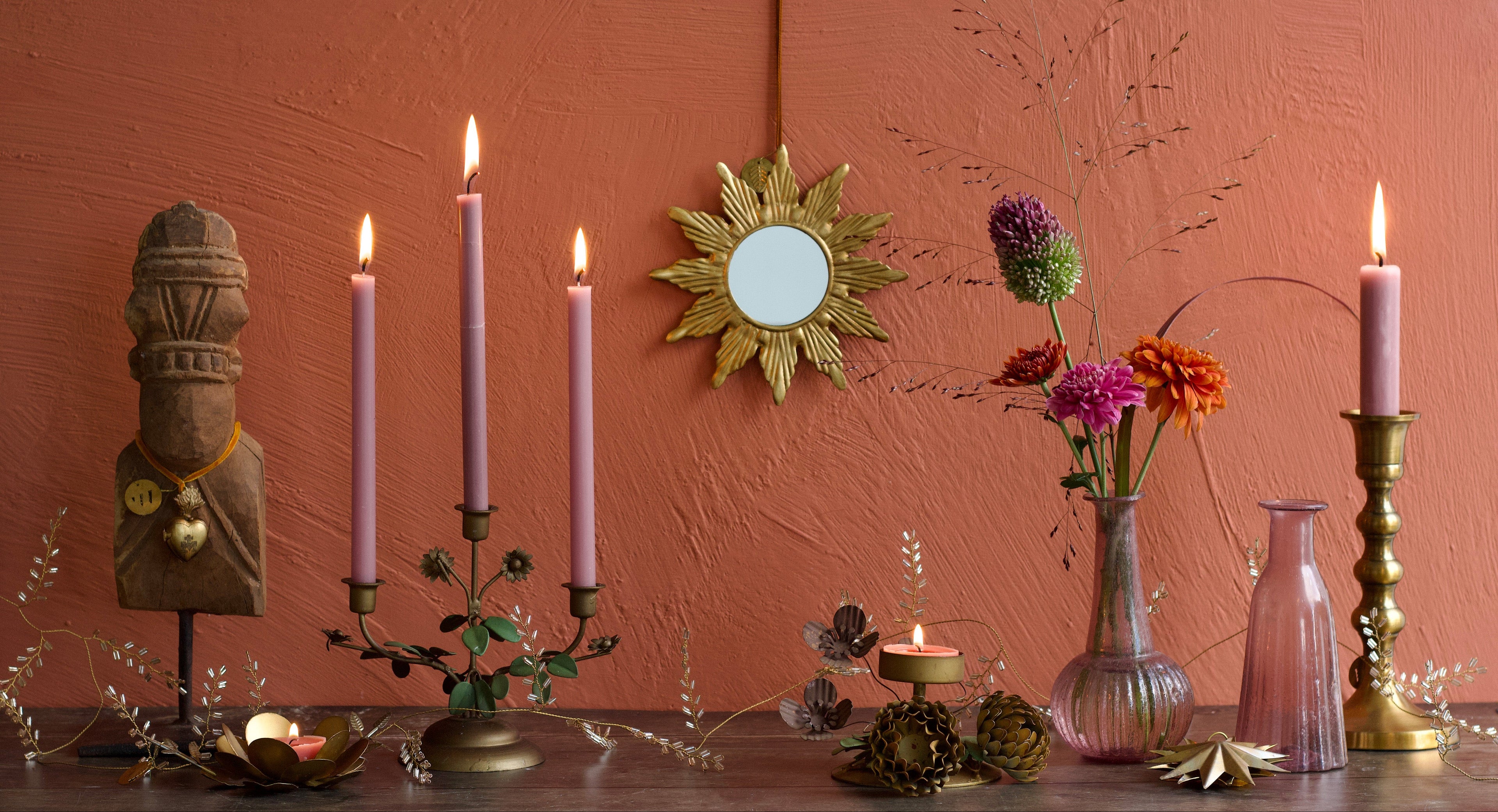 Decorative setup with candles, flowers, and a mirror on a wooden surface against a pink wall.