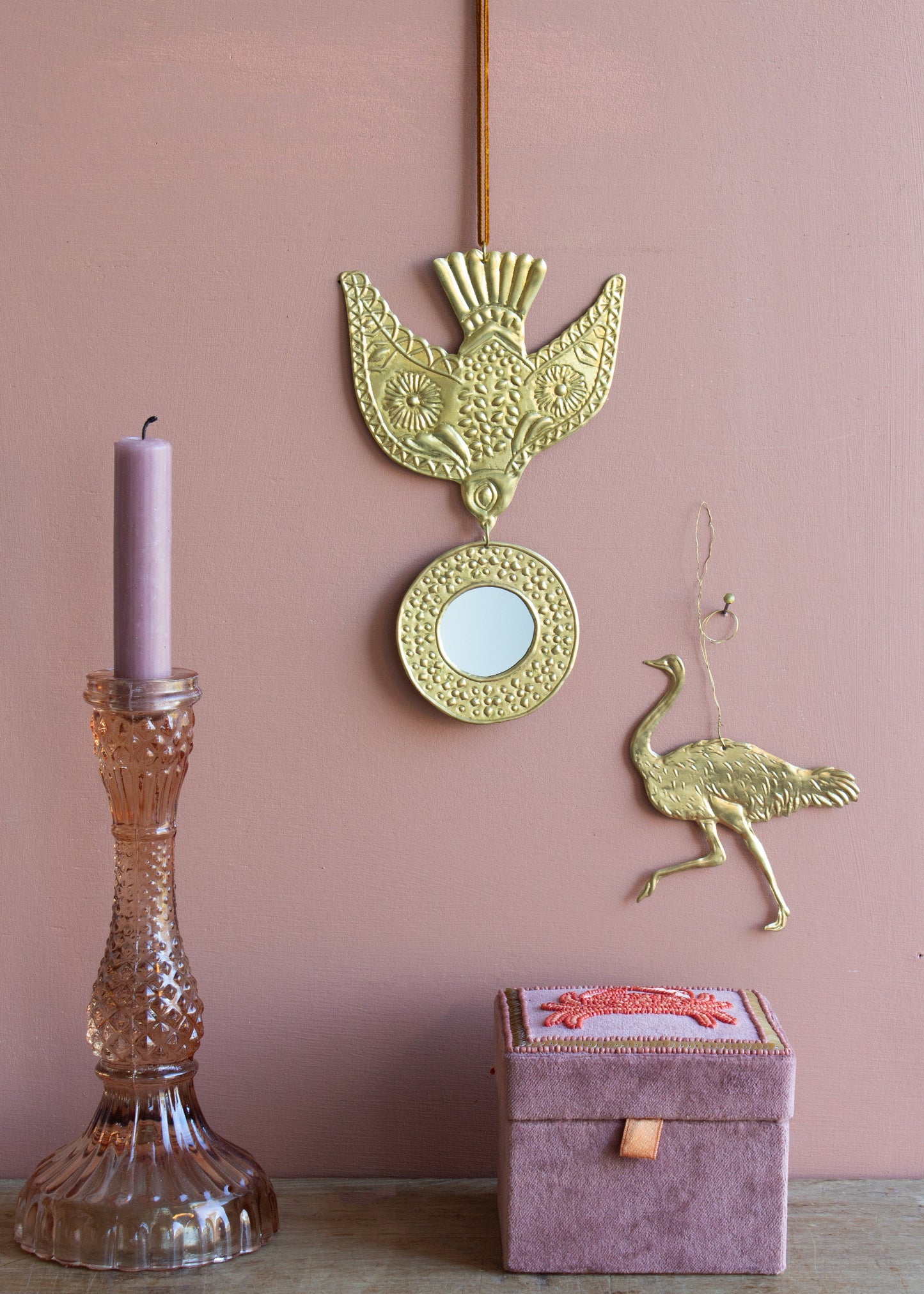 Decorative wall art with a bird design on a pink wall, accompanied by a candle holder and decorative box.