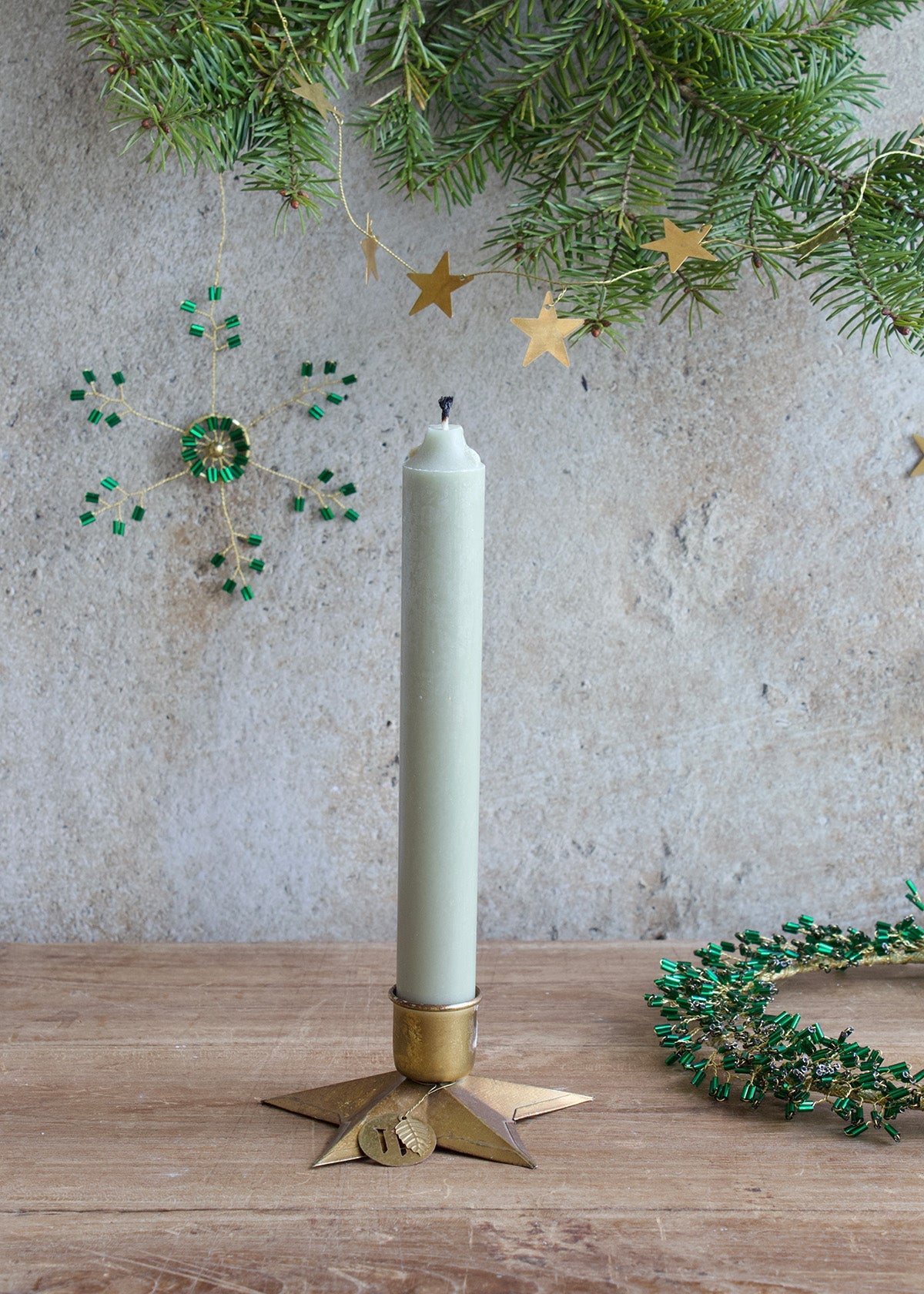 Light green candle in a decorative holder on a wooden surface with festive background.