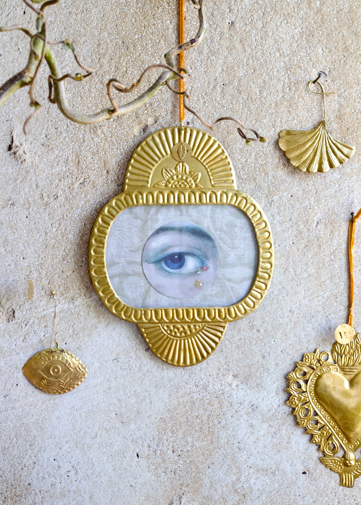 Decorative frame with an eye design surrounded by gold jewelry on a textured surface.