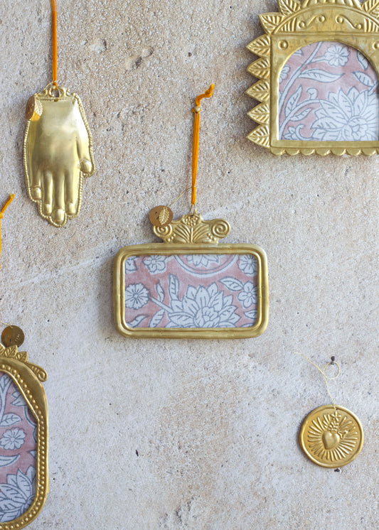 Golden handmade horizontal rectangular ex-voto photo frame with embossed detailing, hanging on a stone wall.