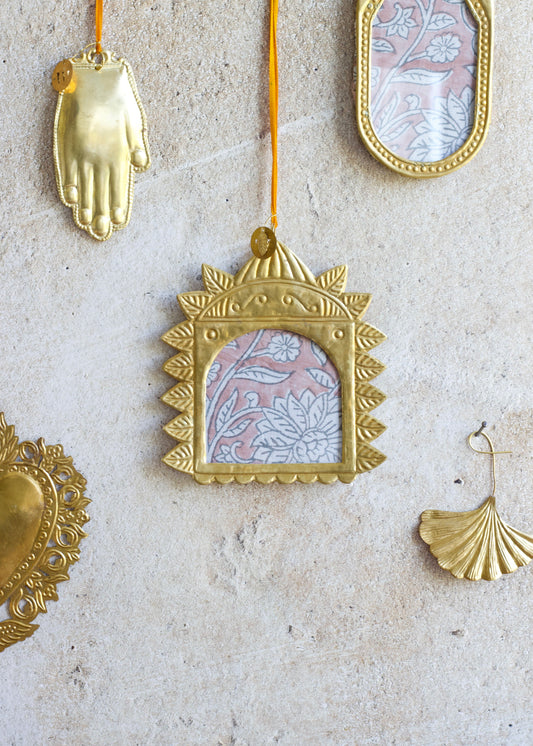 Golden handmade square ex-voto photo frame with embossed sunray border and arched window, hanging on a stone wall.