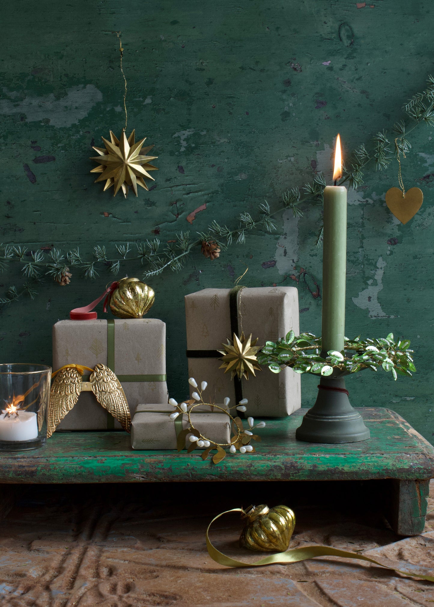 Decorative setup with candles, gift boxes, and ornaments against a textured green wall.
