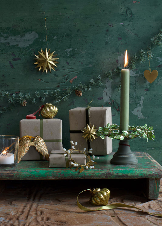 Decorative setup with candles, gift boxes, and ornaments against a textured green wall.