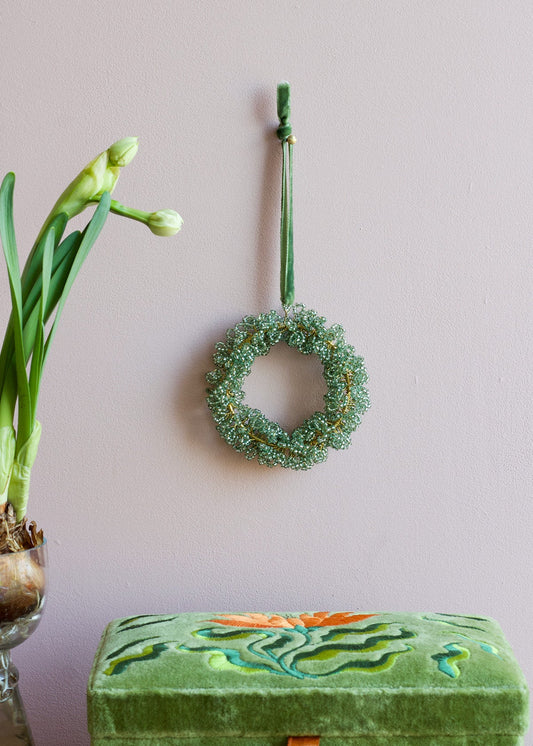 Green wreath hanging on a wall with a vase of flowers and a decorative box below.