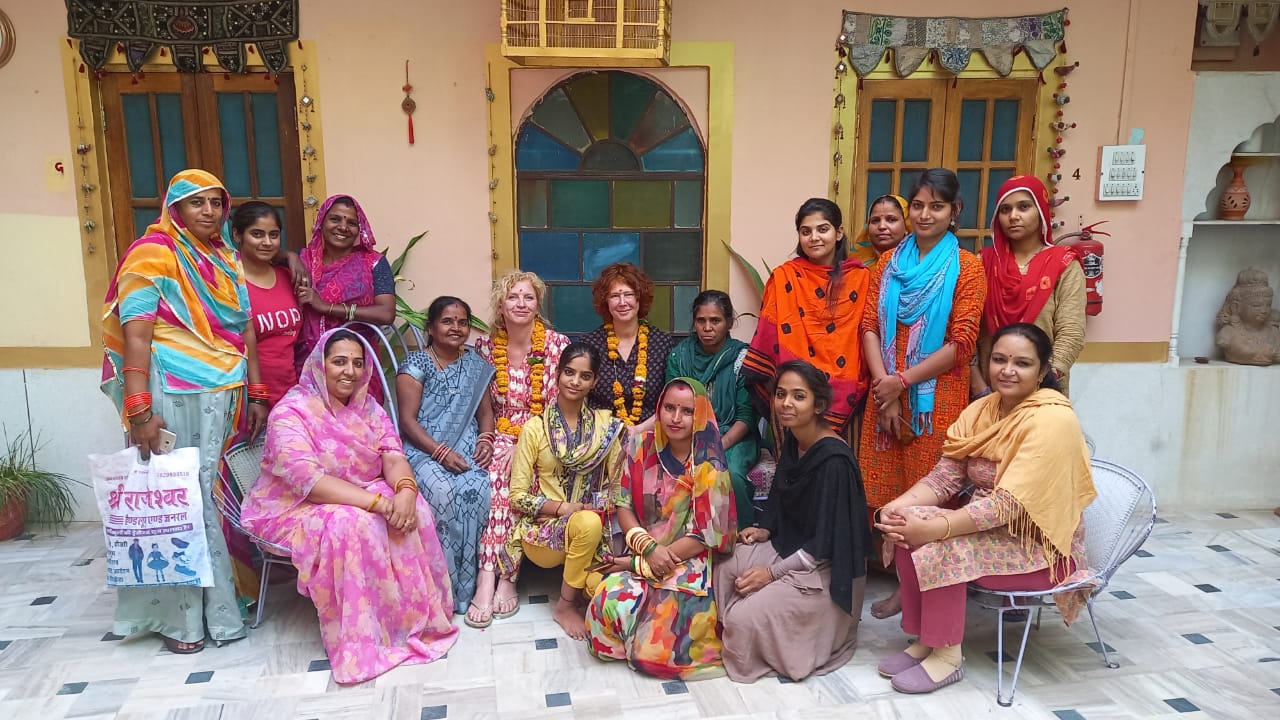 Group of women in colorful traditional attire posing for a photo in a decorated indoor setting.
