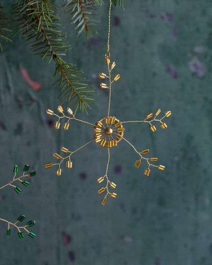Decorative gold ornament hanging from a branch with a textured green background