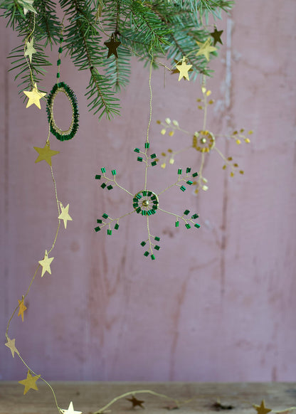 Decorative string with stars and green beads hanging against a pink background