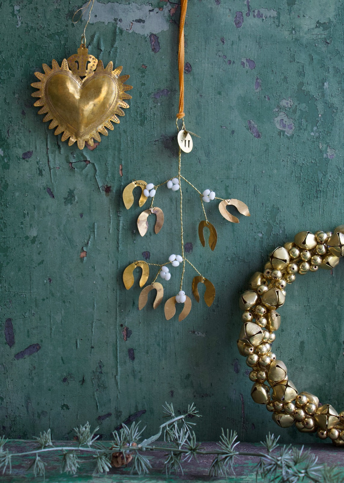 A decorative mistletoe bunch with pearl beads and gold-colored heart-shaped ornaments hanging against a green textured background.