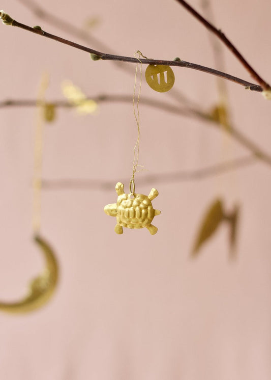 Small gold turtle ornament hanging from a branch with pink background