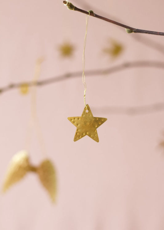 Gold metal star ornament hanging from a twig with a soft pink background.