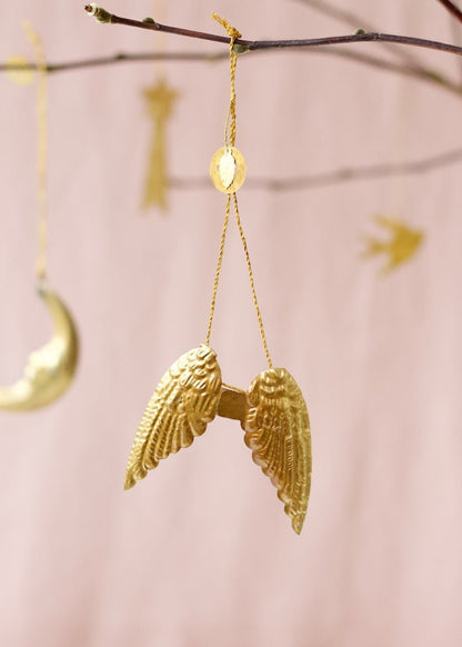 Golden brass angel wings ornament with embossed feather details, hanging from a branch.
