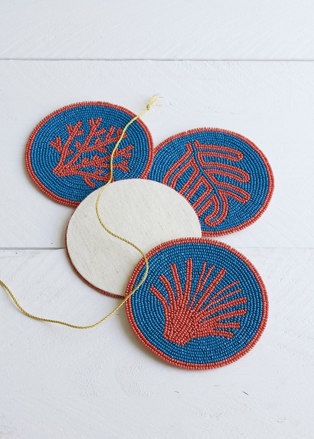 Set of four beaded coasters with coral and shell designs on a white background