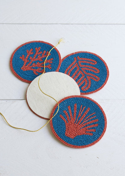 Set of four beaded coasters with coral and shell designs on a white background