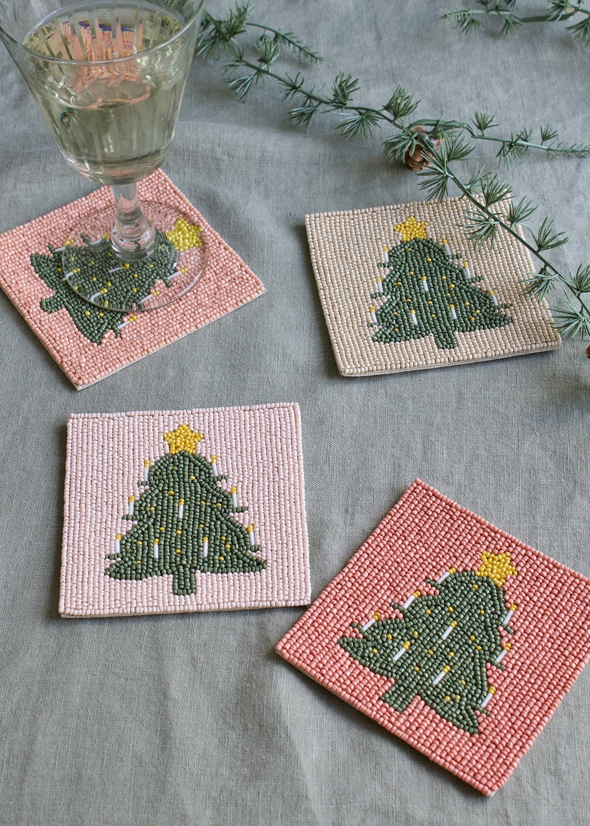 Set of four beaded coasters with Christmas tree design on a gray surface.