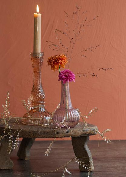 Decorative setup with a candle, vase with flowers, and decorative elements on a wooden surface against a red-brown background.