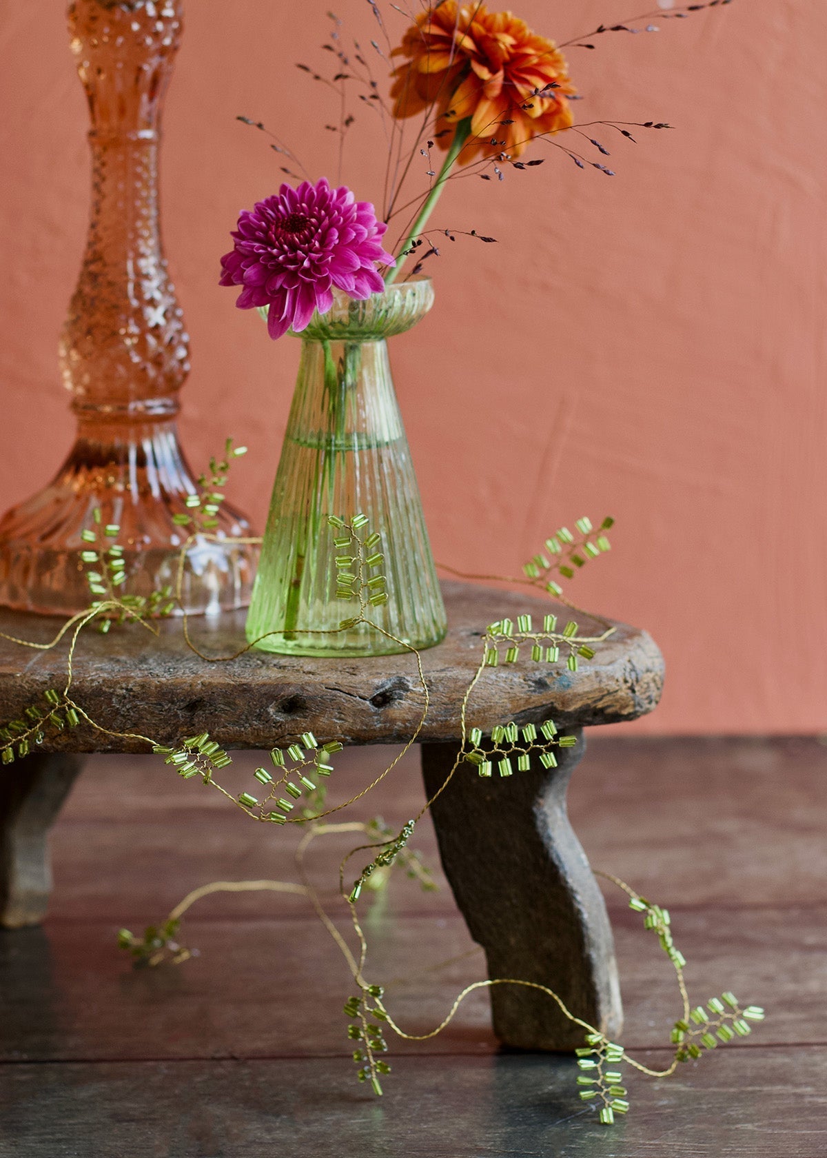 Green vase with flowers on a wooden stool against a pinkish-brown background