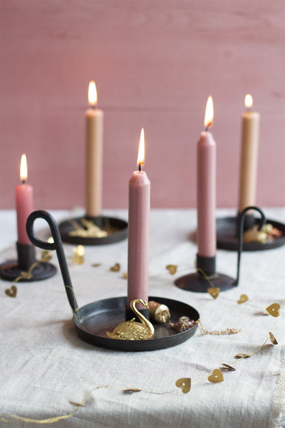 Black iron candle holders with pink taper candles lit on a linen covered table.