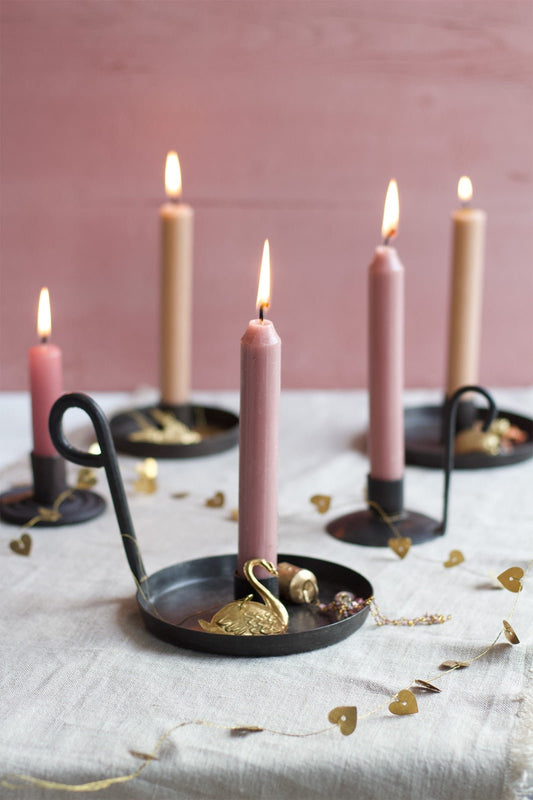 Black iron candle holders with pink taper candles lit on a linen covered table.