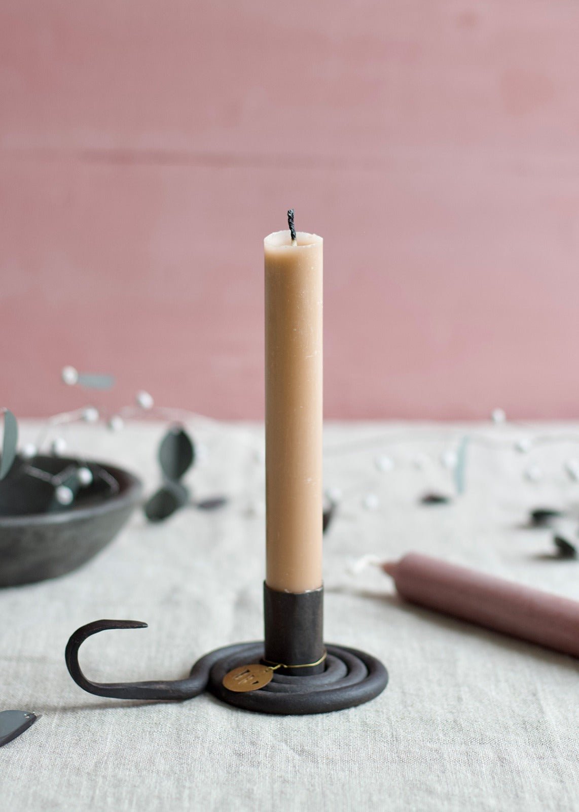Black iron spiral candle holder with a beige taper candle on a linen table.