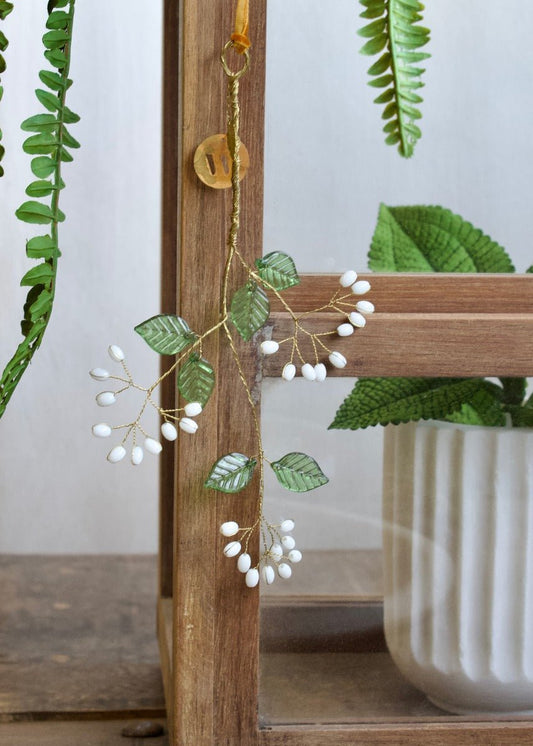 Delicate botanical hanging bunch with green leaves and white beads, attached to a wooden cabinet.