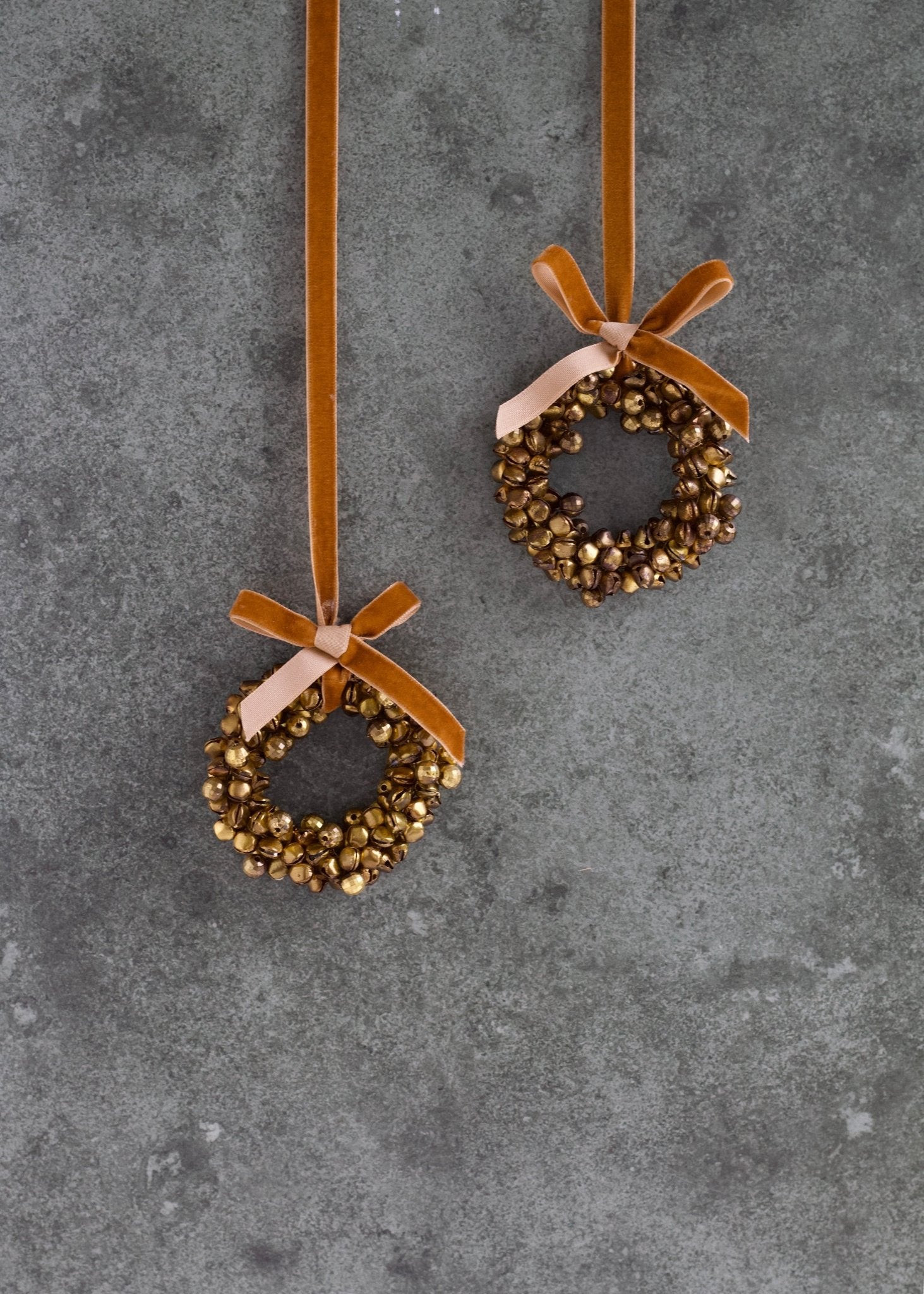 Two decorative wreath ornaments with ribbons on a gray surface