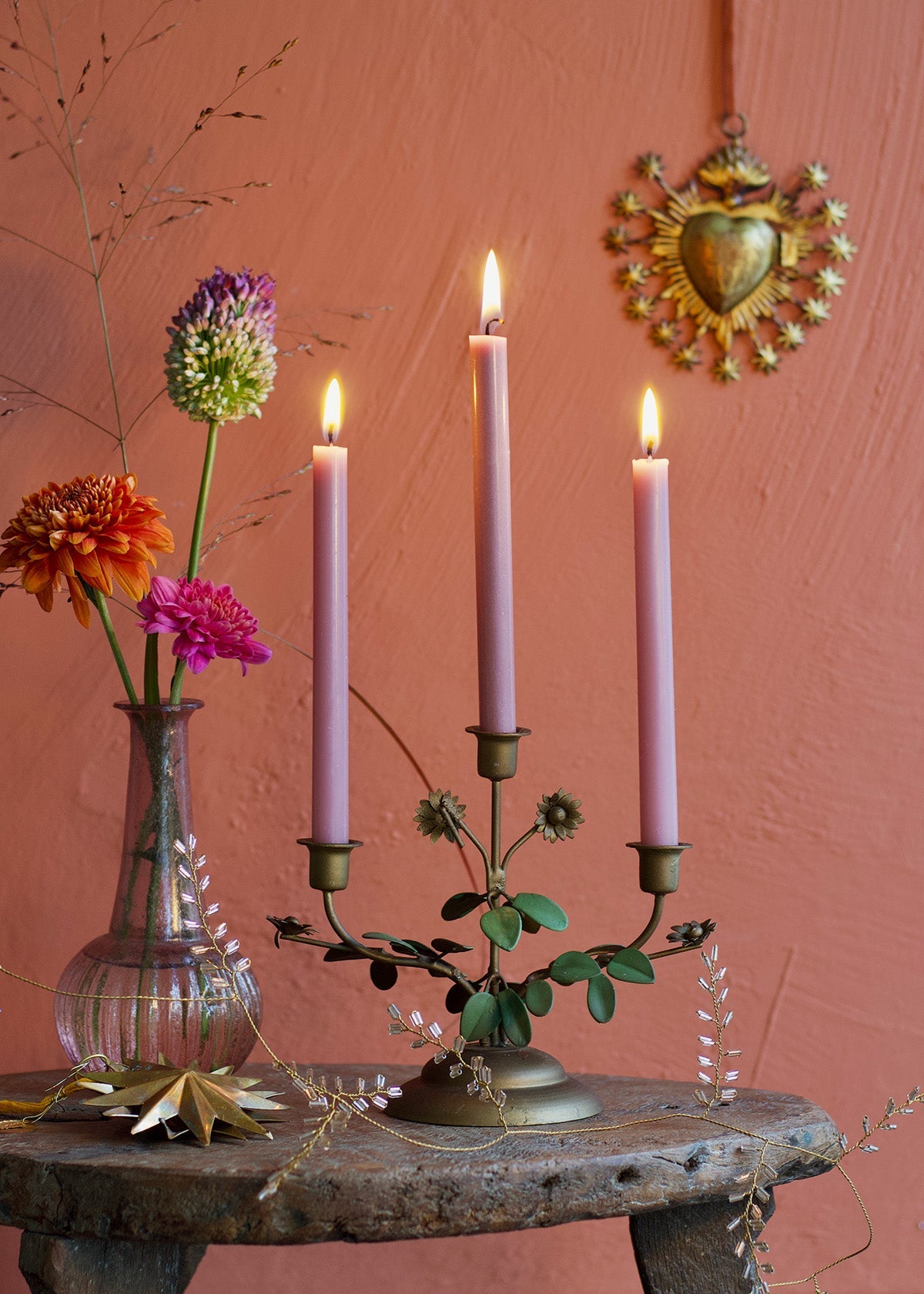 Candlestick with lit candles on a rustic table against a pink wall with decorative elements.
