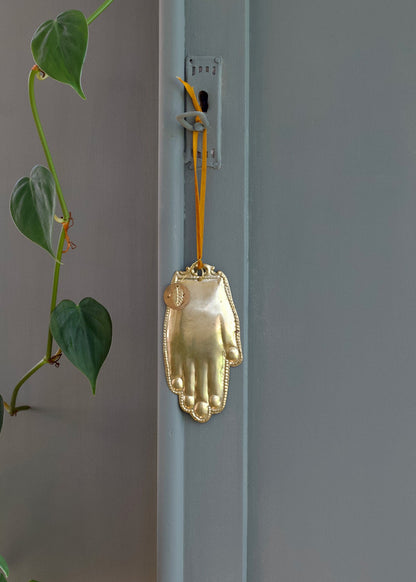 Gold hand-shaped ornament hanging on a light blue door with green leaves in the background