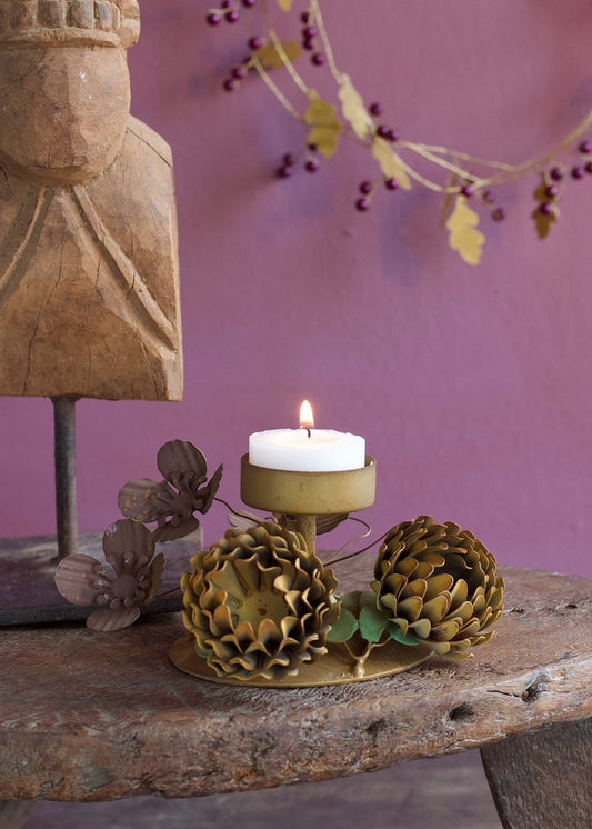 Brass tea light holder with hand-shaped metal flowers and a lit candle placed on a rustic wooden table against a mauve wall.