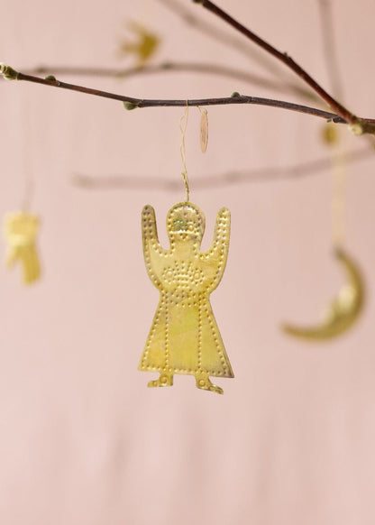 Brass gingerbread figure ornament with dotted embossing, hanging from a twig against a soft pink background.