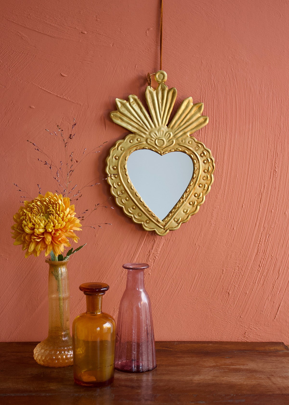 Heart-shaped gold mirror on a pink wall with decorative vases and flowers.