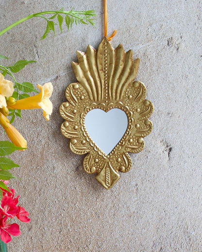 Decorative gold heart-shaped mirror on a textured wall with flowers and fabric in the foreground.