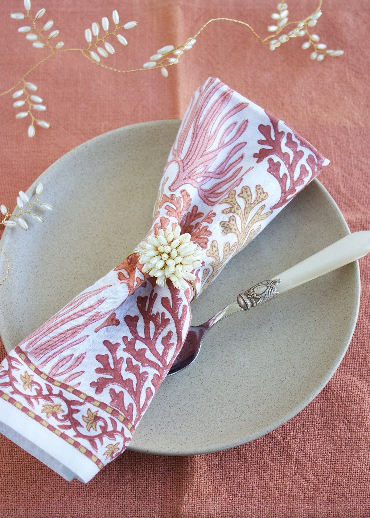 Decorative napkin with coral and gold pattern on a plate with a fork, on a pink tablecloth.