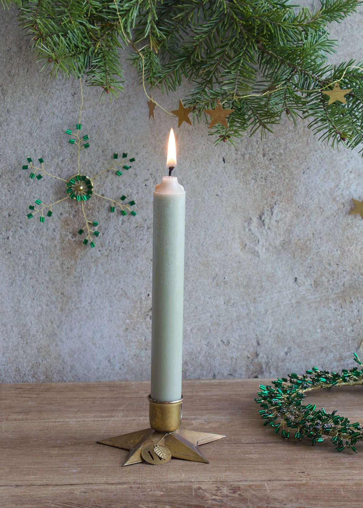 Lighted candle in a decorative holder with greenery and stars in the background