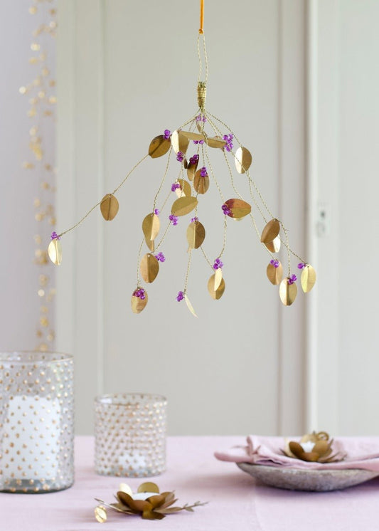 Brass hanging garland with gold leaves and purple beads, suspended above a pink-decorated table with candle holders and plates.