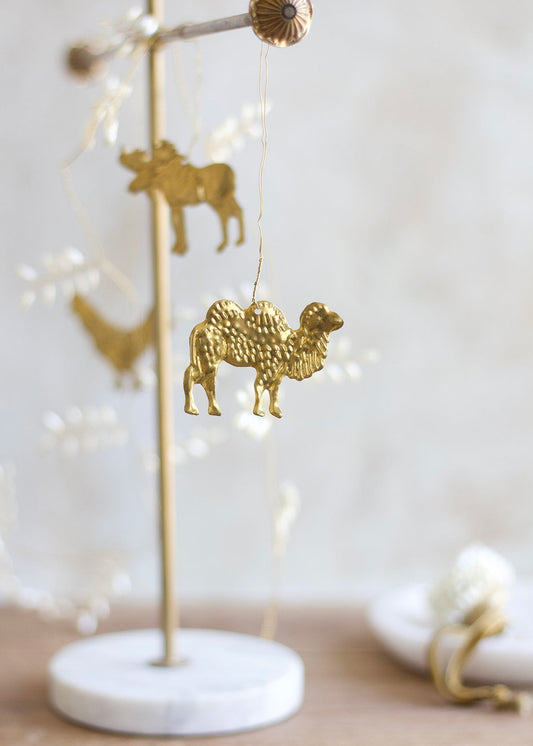 Brass camel ornament hanging from a decorative wire garland with a marble stand and softly blurred background.