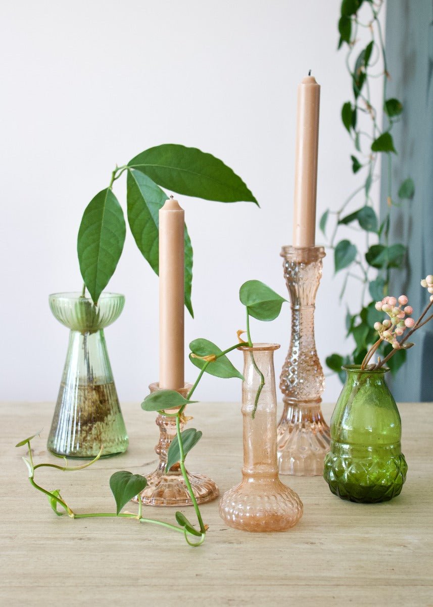 Decorative vases and candles on a wooden surface with plants in the background