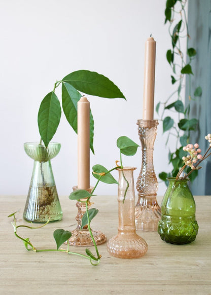 Decorative vases and candles on a wooden surface with plants in the background