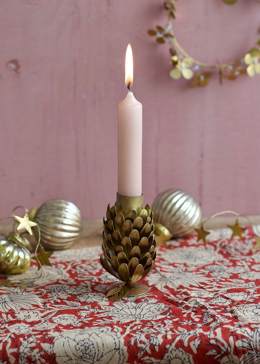 Decorative candle holder with a lit candle on a tablecloth with Christmas decorations.