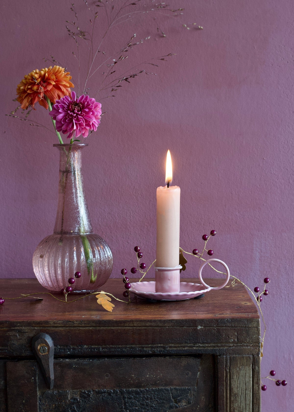 Candle and vase with flowers on a wooden surface against a purple wall