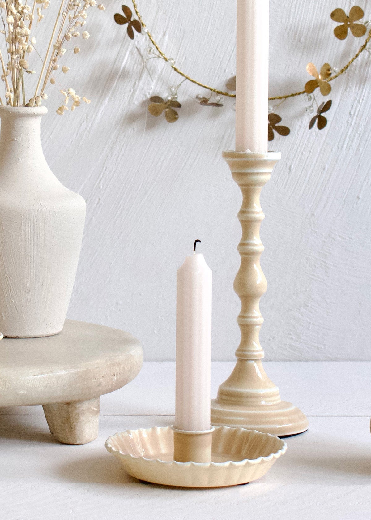 Decorative setting with candles, a vase, and a shell-shaped candle holder on a light background.