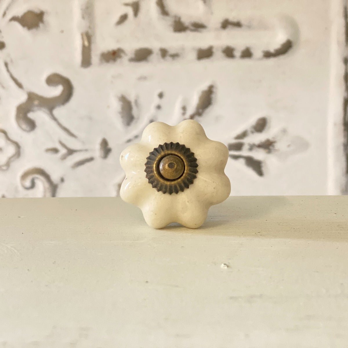 A white, flower-shaped cabinet knob with a brown center, displayed against a wall with a decorative pattern.