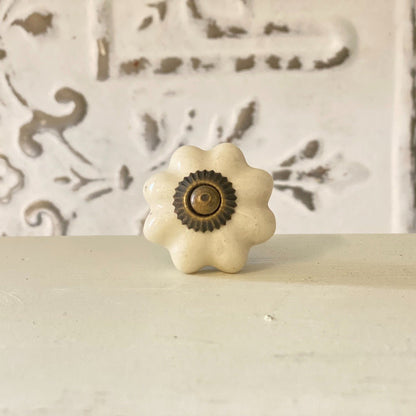A white, flower-shaped cabinet knob with a brown center, displayed against a wall with a decorative pattern.