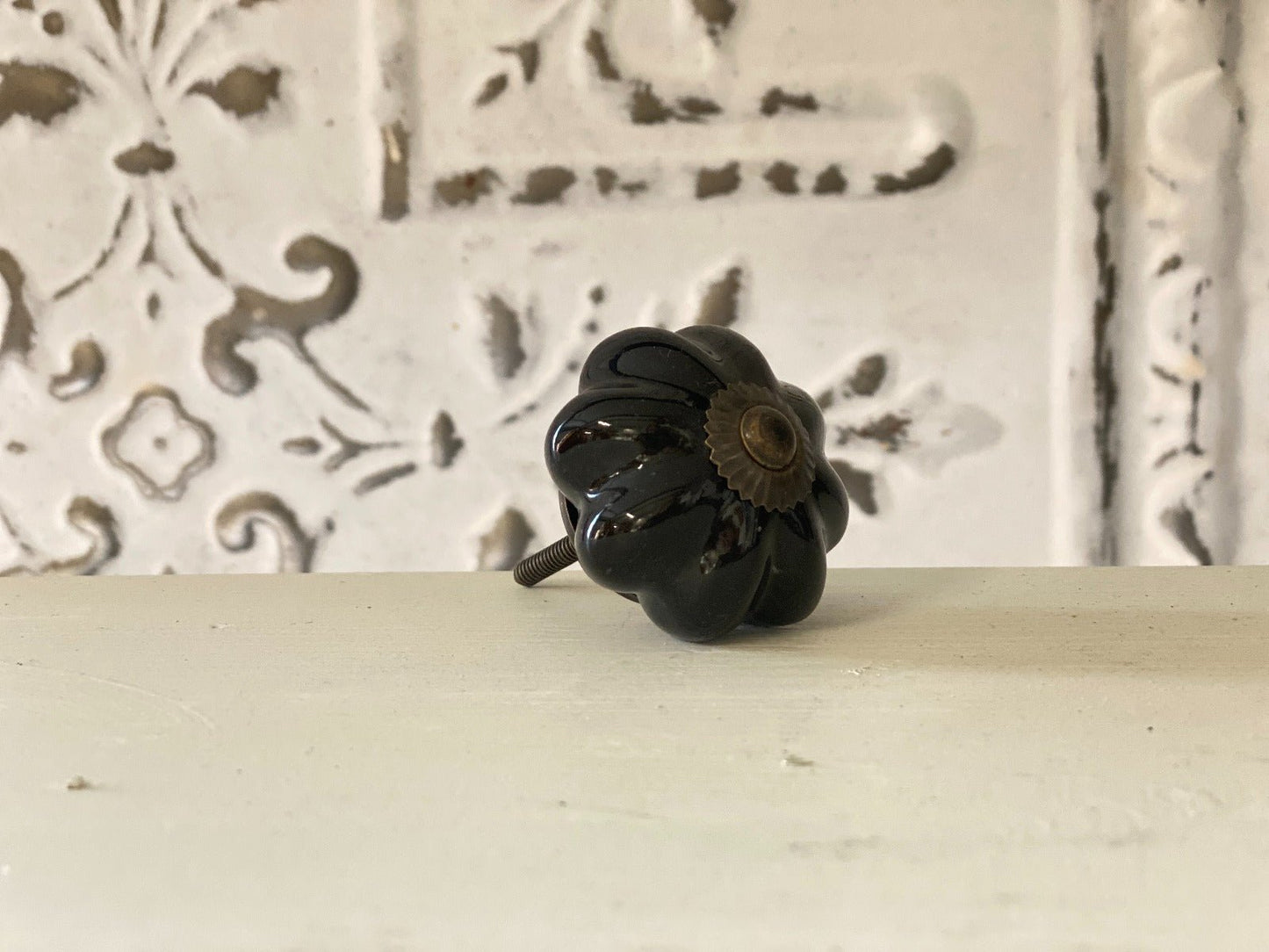 A black, curved cabinet knob against a white decorative background.